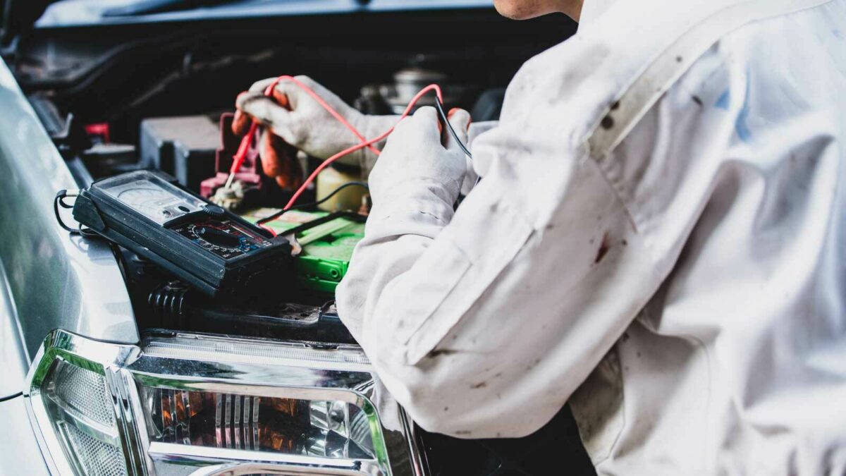 Mechaniker überprüft mit einem Multimeter die Spannung einer Autobatterie.